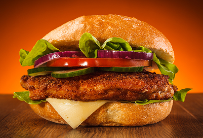 A fried chicken sandwich with lettuce, onion, tomato, pickle and cheese.